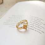 A gold ring with a triangular gold top, resting on an open book with printed text.