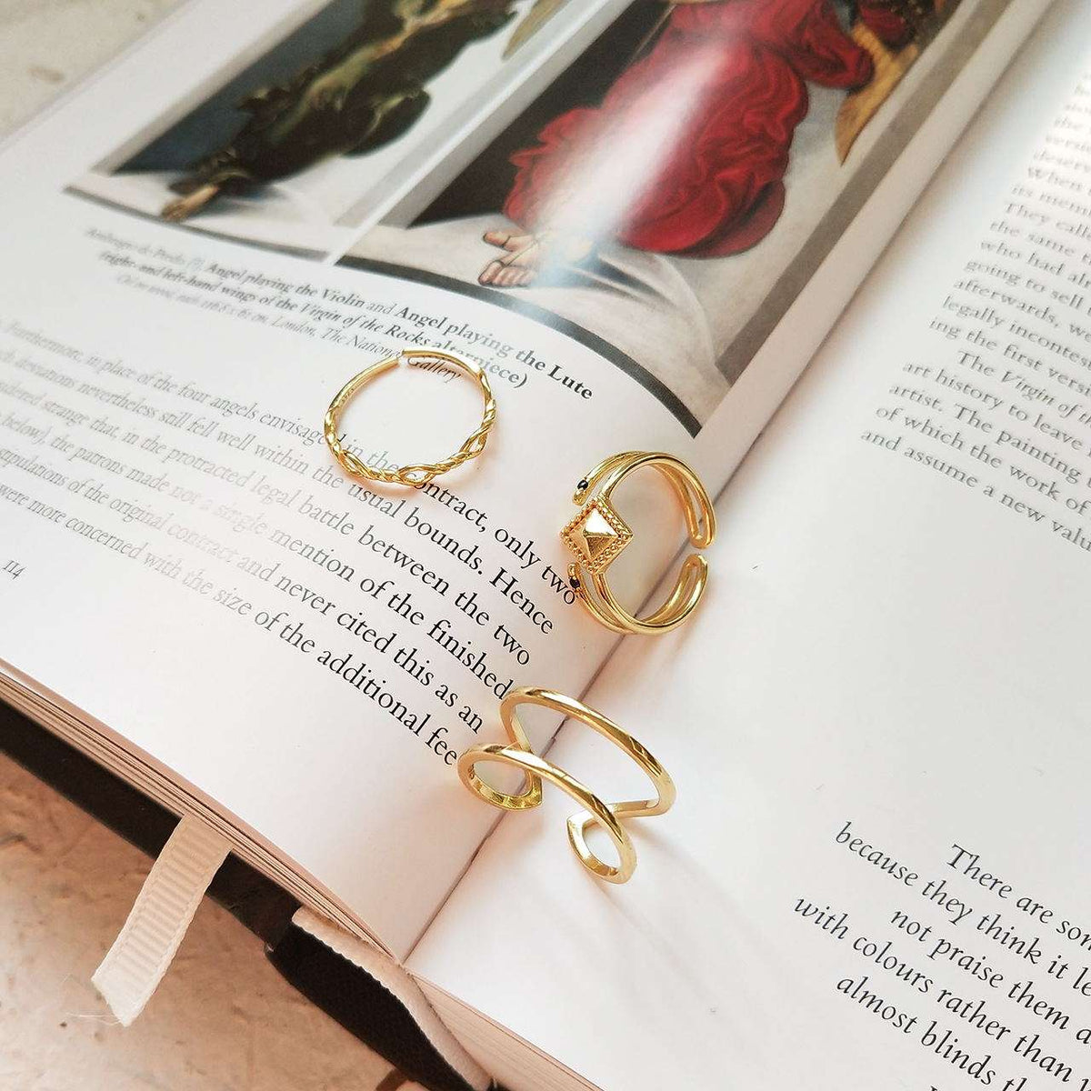 Three gold rings with unique textured and geometric designs, displayed on the pages of an open book.