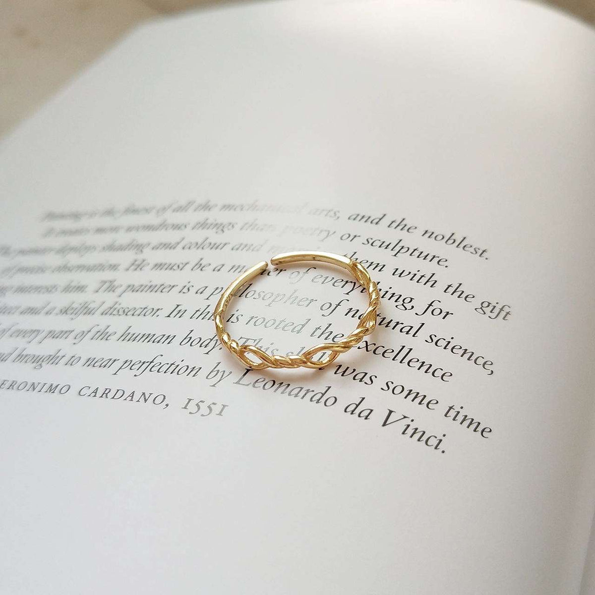 A thin gold ring with a textured, organic wavy design rests on the pages of an open book.
