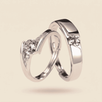 Two polished silver wedding bands with round-cut clear gemstones, shown interlocking on a warm beige background.