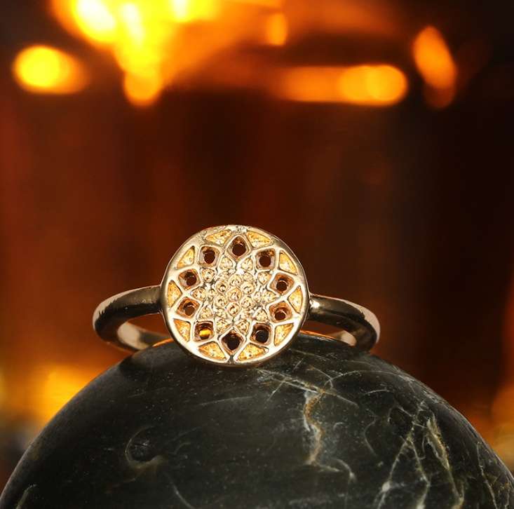 Gold ring with intricate design on a dark stone surface with a warm, blurred background