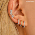Close-up of an ear wearing sparkling stud earrings with 'SparkleSway' branding.