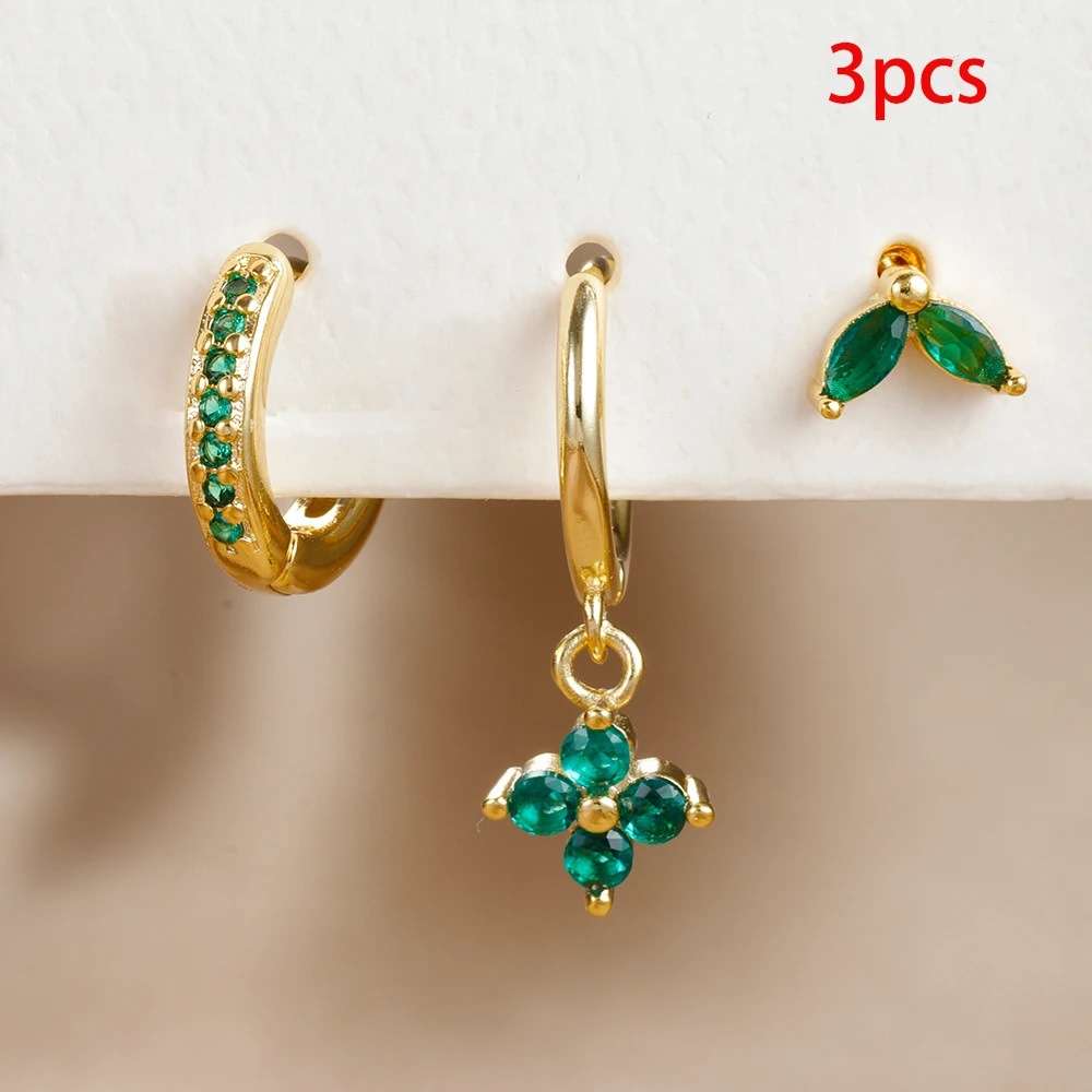 Gold hoop earrings with green gemstones on a beige background