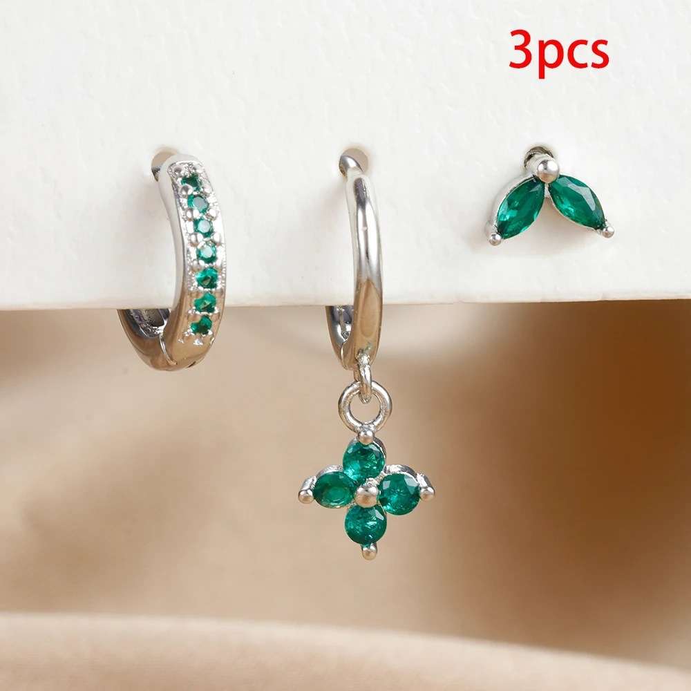 Set of three pairs of green gemstone earrings on a beige surface with a white background.