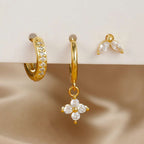 Gold hoop earrings with clear crystal accents, including one huggie hoop with a row of crystals, one hoop with a dangling flower-shaped crystal cluster, and a small matching crystal stud, displayed on a white surface with a beige satin background.
