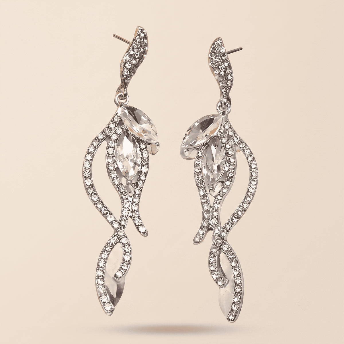A pair of silver-toned dangle earrings with marquise-cut clear crystals and pavé-set rhinestones in a swirling leaf-like design, shown on a solid beige background.