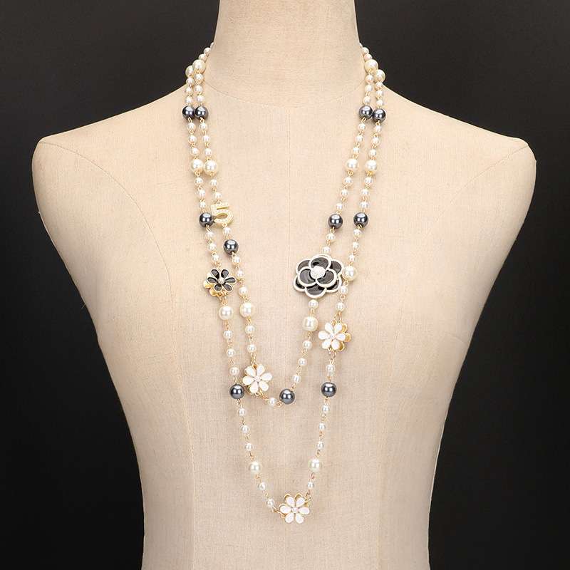 A multi-strand pearl necklace with silver and gold floral charms, displayed on a beige fabric mannequin torso against a black background.