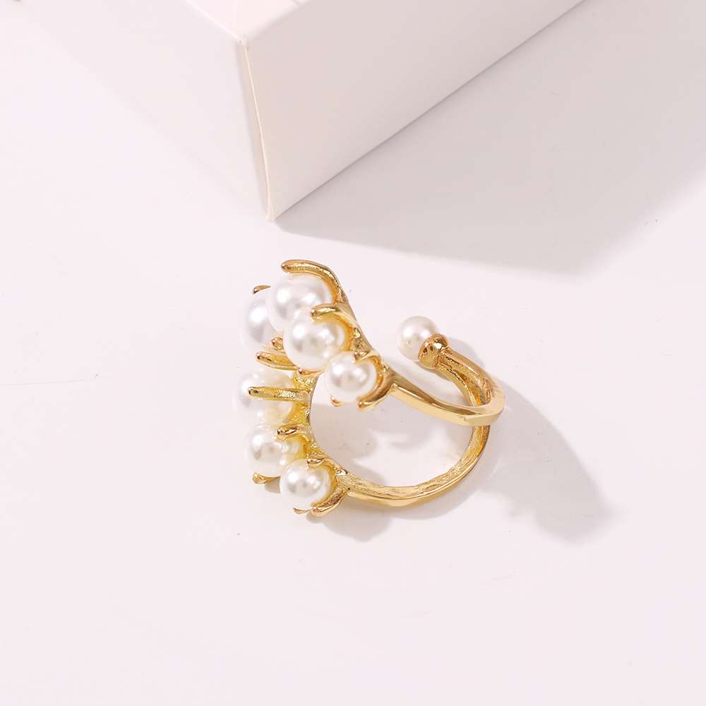 A gold-plated ring designed to look like a cluster of white pearls on a branch, photographed on a clean white surface with a white geometric block in the background.