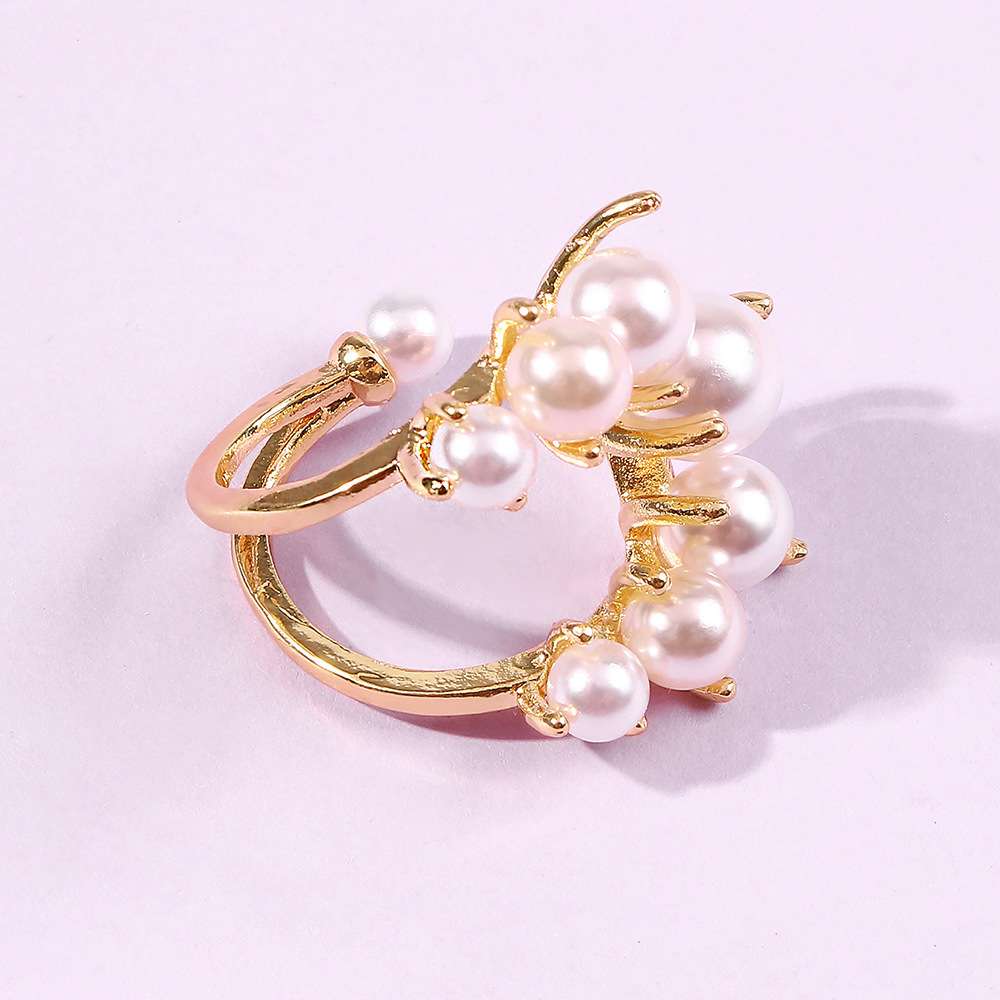 A gold-plated ring featuring a cluster of white faux pearls on a light pink background.