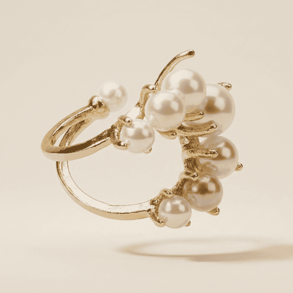 A gold ring featuring a cluster of white faux pearls set in a branch-like design, shown on a warm beige background.