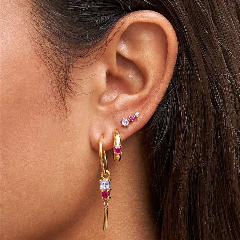 Close-up of an ear wearing gold hoop earrings with gemstones.