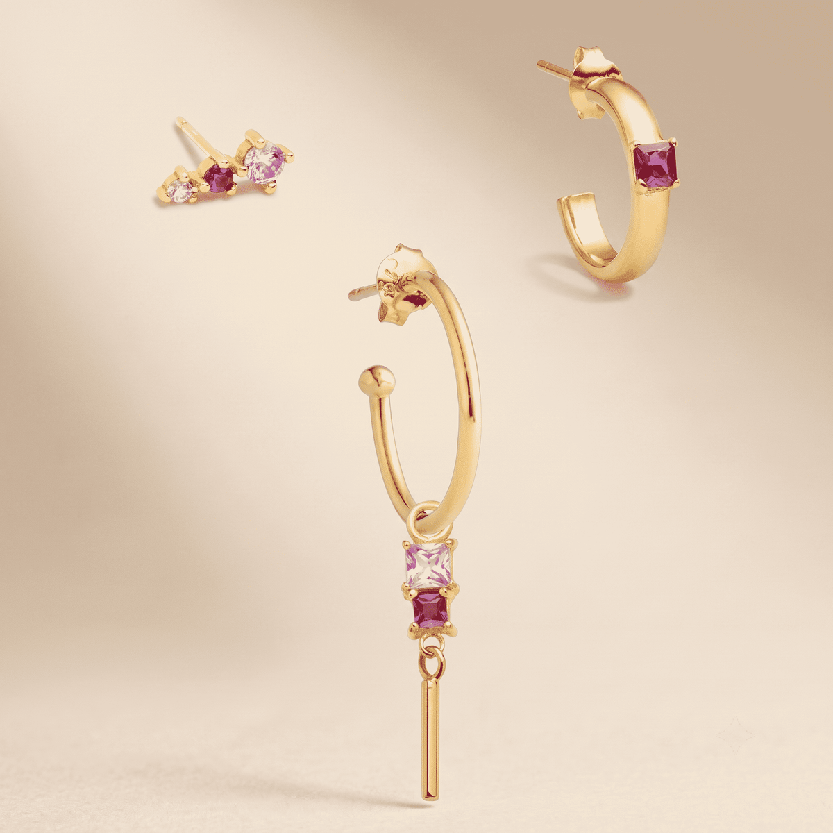Gold hoop earrings with pink and clear gemstones, shown in multiple views on a warm beige background.