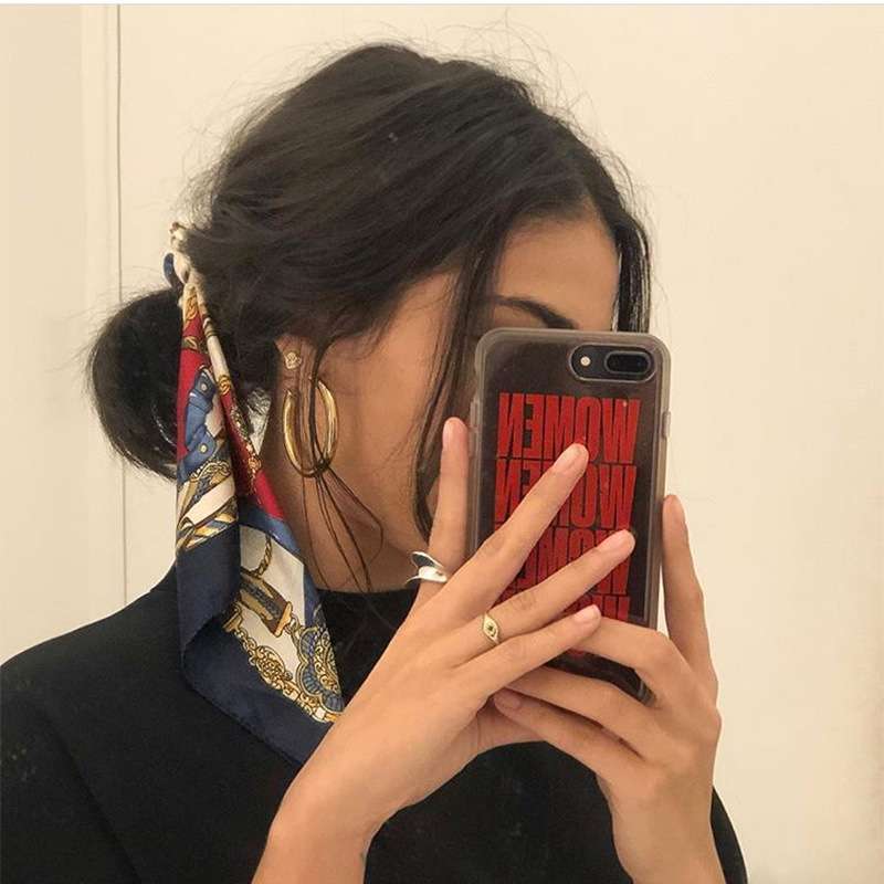 Person holding a phone with a red and black case, wearing a patterned scarf and large hoop earrings.