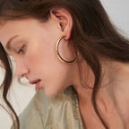 Close-up of a person wearing a gold hoop earring with a neutral background