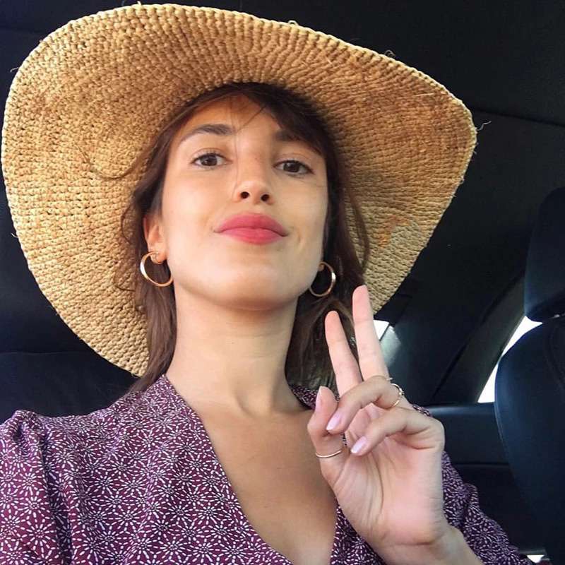 Woman wearing a straw hat and making a peace sign inside a car.