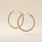 A pair of thick, polished gold hoop earrings floating against a warm beige background.