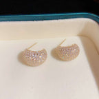 Gold earrings with gemstones on a white cushion in a jewelry box.