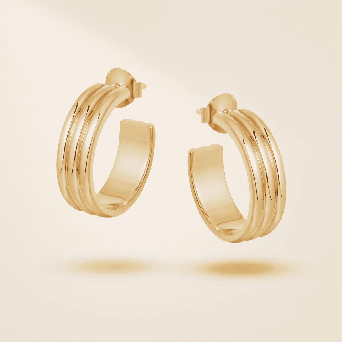 A pair of gold hoop earrings with a multi-band twisted design, shown floating against a warm cream background.