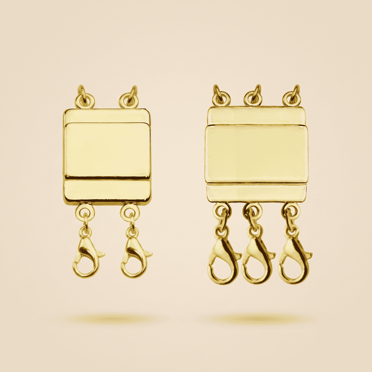 Two gold-toned rectangular connector pieces with three lobster claw clasps hanging from each piece, shown on a plain warm beige background.