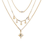 A gold-toned multi-layer necklace set featuring three distinct chains: a delicate cable chain, a thin chain with a small round clear stone, and a star-themed chain with five dangling star charms and a larger starburst pendant with a clear center stone.