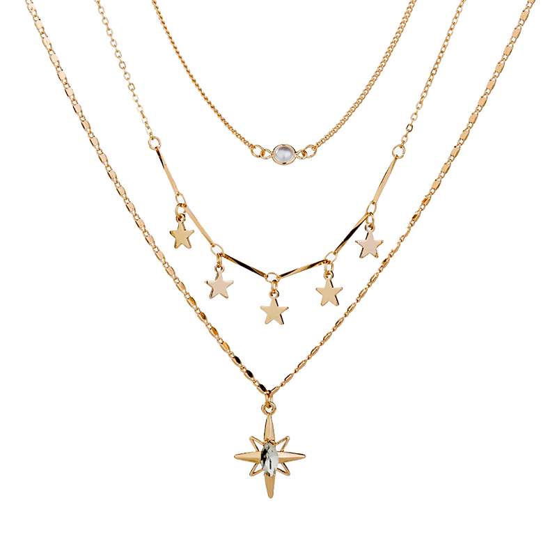A gold-toned multi-layer necklace set featuring three distinct chains: a delicate cable chain, a thin chain with a small round clear stone, and a star-themed chain with five dangling star charms and a larger starburst pendant with a clear center stone.