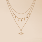 A rose gold multi-layer necklace featuring star and lightning bolt charms, with a larger starburst pendant, displayed against a solid beige background.
