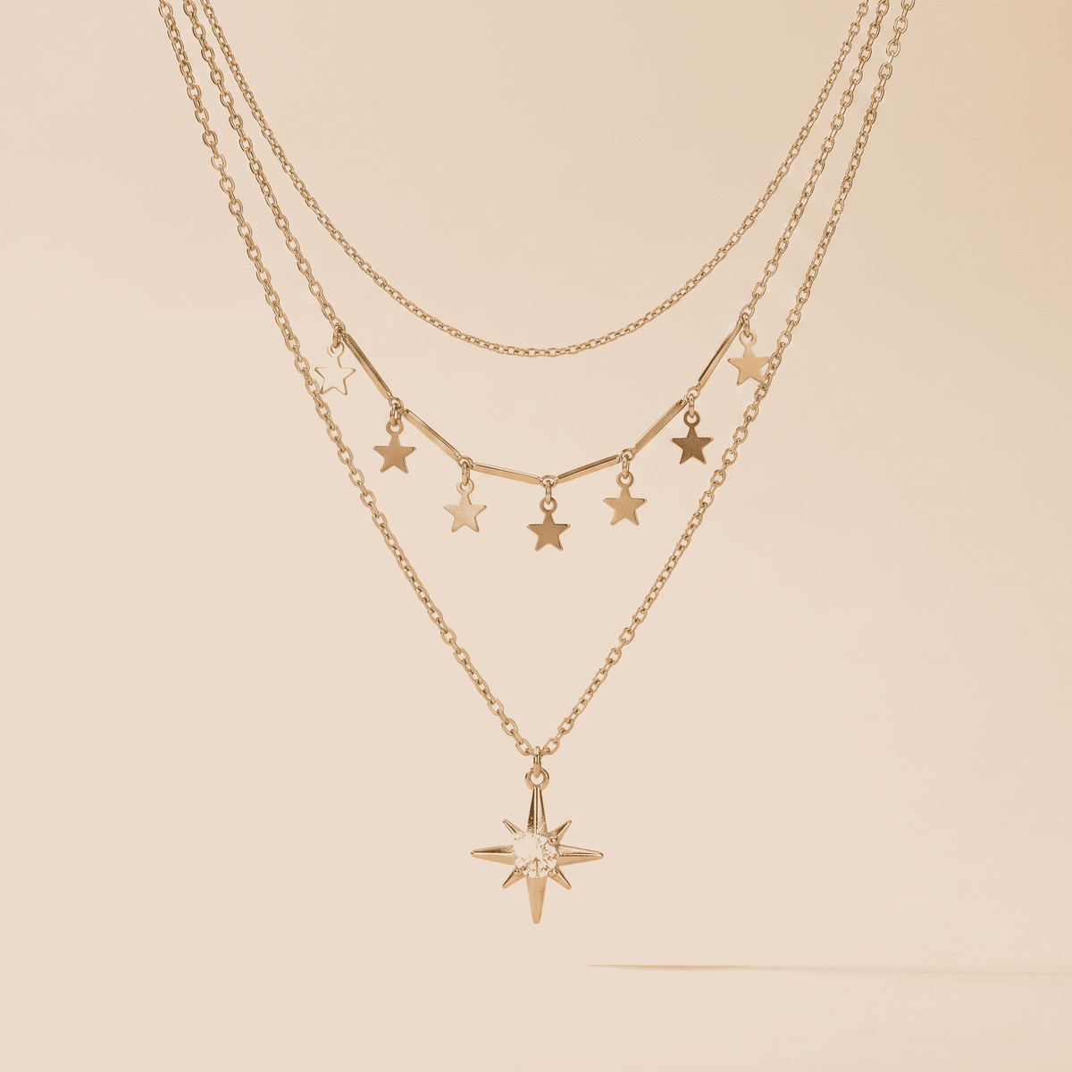 A rose gold multi-layer necklace featuring star and lightning bolt charms, with a larger starburst pendant, displayed against a solid beige background.