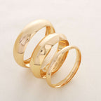 Three polished gold rings arranged in a spiral stack on a light off-white background.
