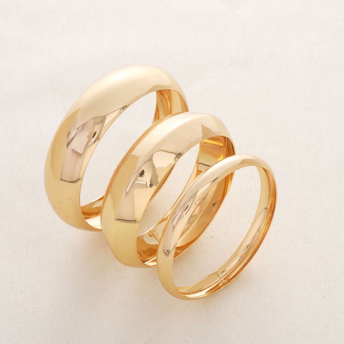 Three polished gold rings arranged in a spiral stack on a light off-white background.