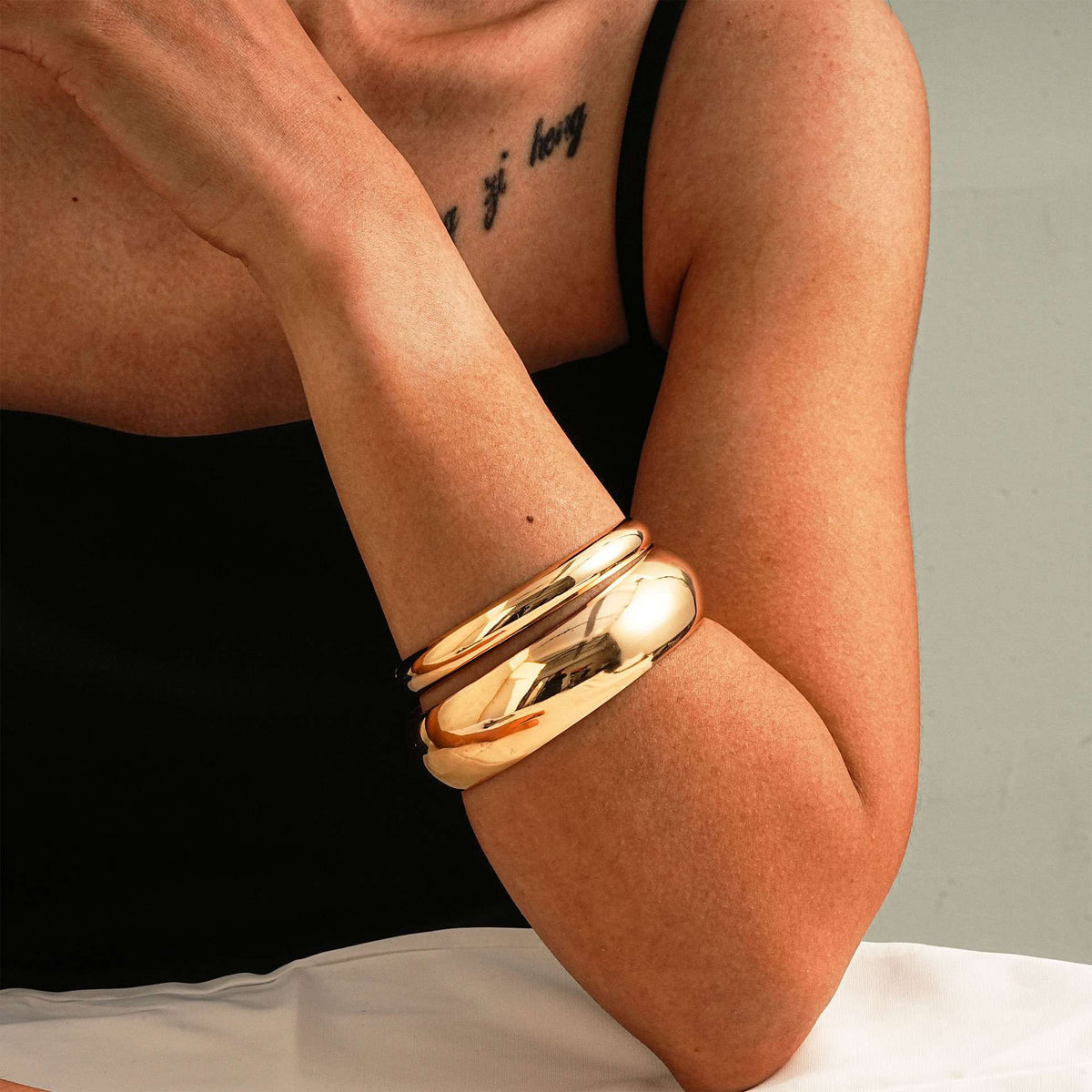Gold bangles on a person's wrist with a neutral background