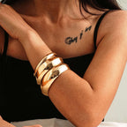 Close-up of a person's arm wearing gold bracelets with a tattoo on the chest.