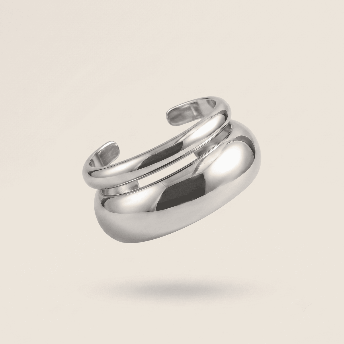 A polished silver-toned metal ring with a modern, fluid, multi-layered curved design, shown floating against a solid light beige background.