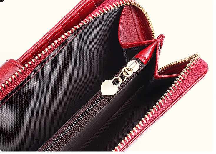 Close-up of a red leather zip-around wallet or clutch with a black interior lining and gold-tone zipper hardware, including a heart-shaped zipper pull.