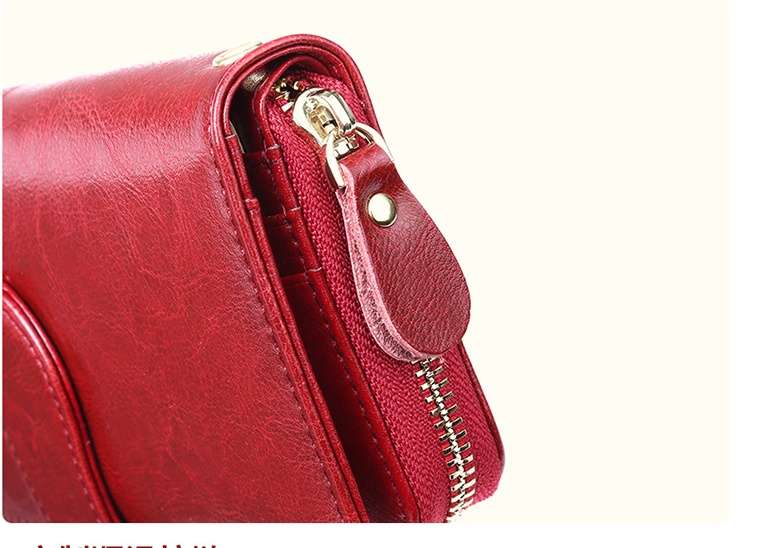 A close-up detail shot of a red faux-leather crossbody bag showing the side zipper, gold-tone metal hardware, and a matching red leather pull tab against a light cream background.