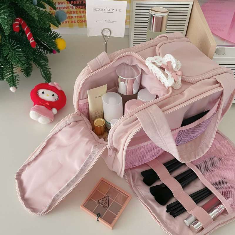 Pink makeup bag with cosmetic items on a desk