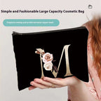 Black cosmetic bag with floral design and letter 'M' held by a person