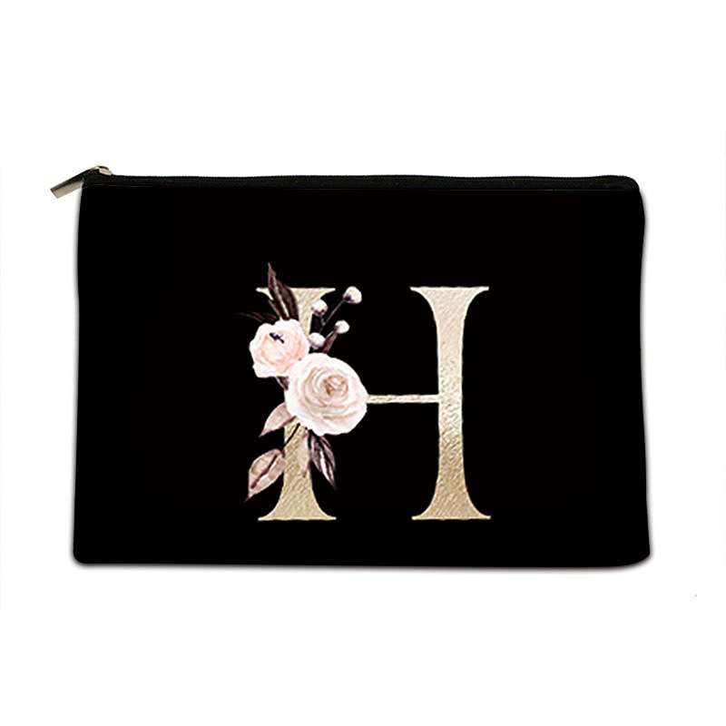 A black zippered pouch featuring a large metallic gold letter 'H' embellished with light pink and white roses, set against a plain white background.