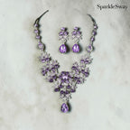 Purple jewelry set with necklace and earrings on a textured surface, branded 'SparkleSway'.