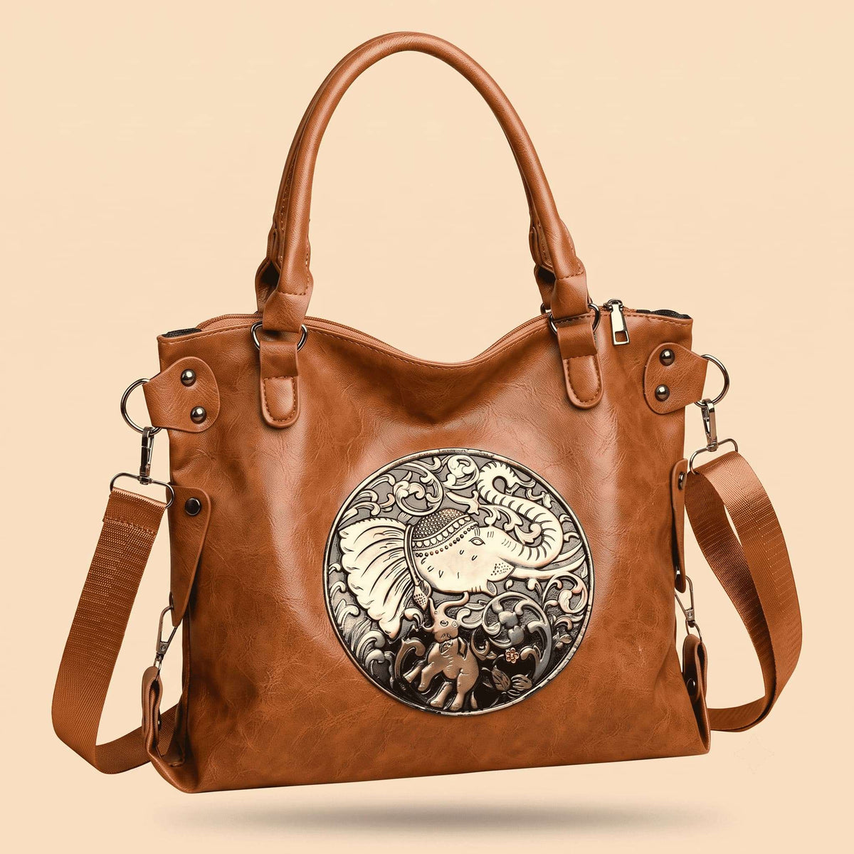 A brown leather handbag with a large circular silver-toned elephant emblem on the front, dual top handles, and an adjustable shoulder strap, shown on a plain beige background.