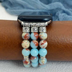 Multiple beaded bracelets on a wrist with a watch, against a blue fabric background