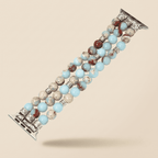 A beaded watch band with light blue, brown, and cream marbled beads, accented with silver-toned spacer beads and decorative silver-toned metal clasp ends, shown on a solid beige background.
