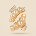 Two translucent beige hair claw clips decorated with large white faux pearls, floating against a solid light beige background.