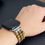 A close-up of a person's wrist wearing a black smartwatch with a decorative multi-strand bracelet featuring brown wooden beads and ornate silver-toned metal accents.