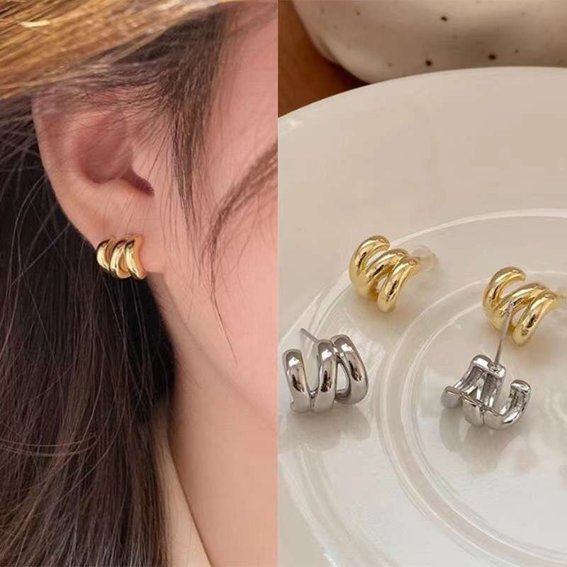 Gold and silver hoop earrings displayed on a clear stand with a close-up of an ear wearing a gold earring.