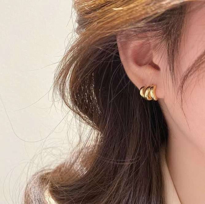 A close-up of a person's ear wearing a small gold hoop earring with three stacked curved bands.