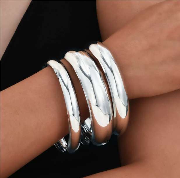 Silver bangles on a wrist against a black background