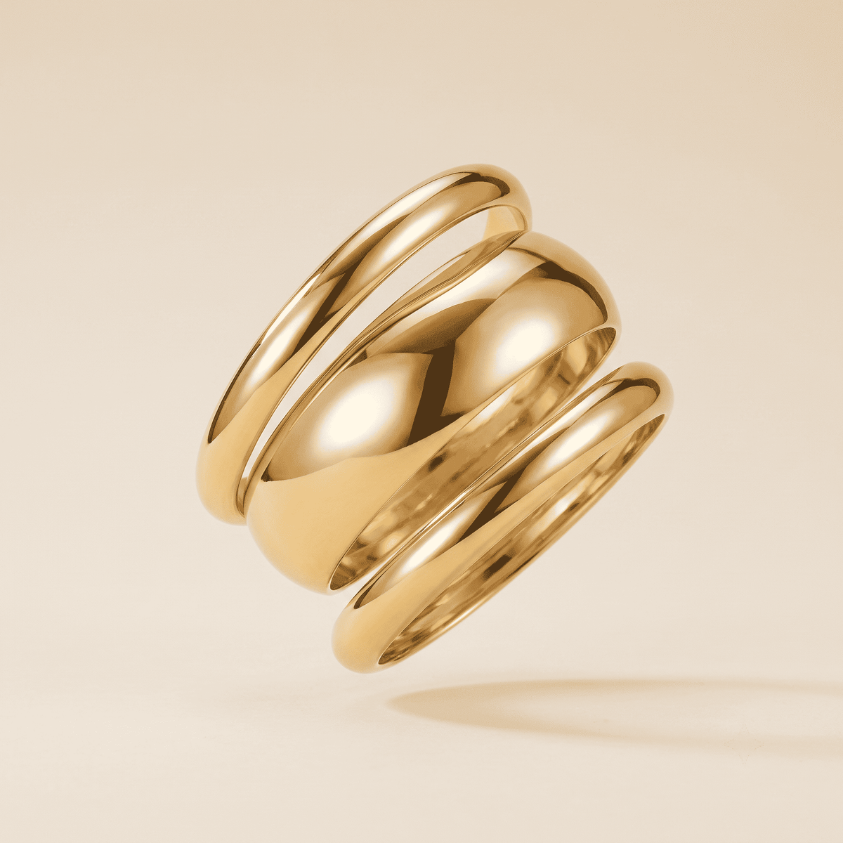 A polished gold multi-band ring floating at an angle against a warm beige background.
