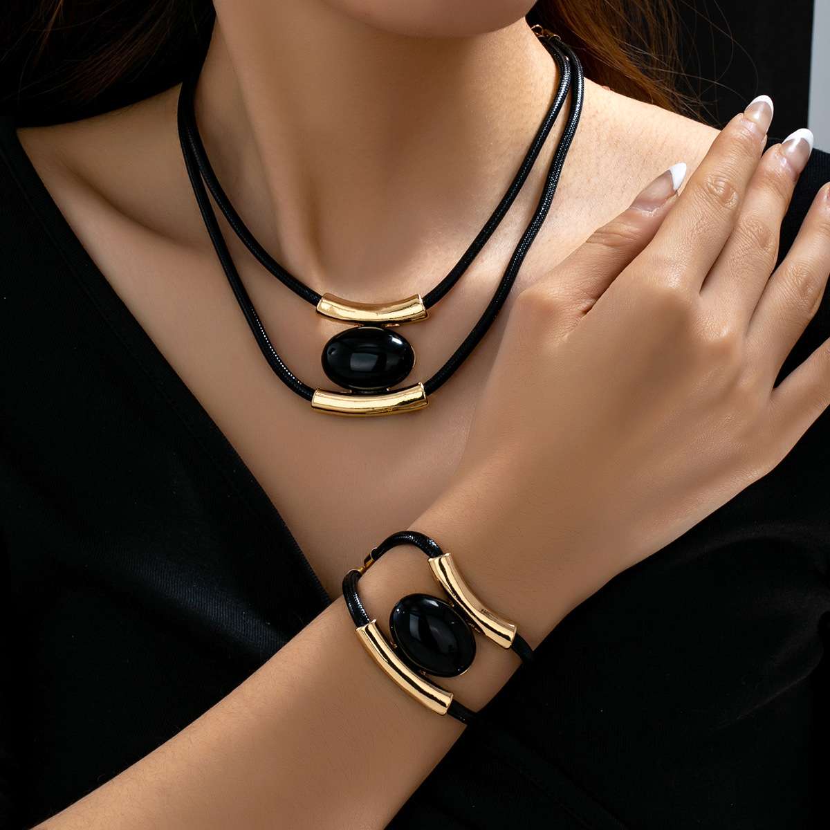 Black and gold jewelry set with necklace and bracelet on a model against a dark background